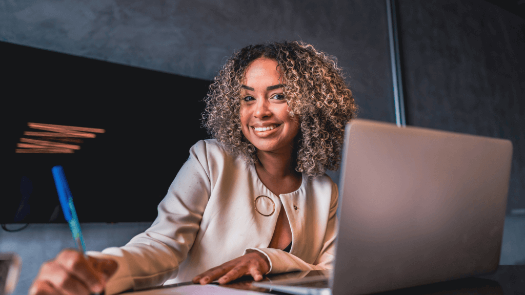 Femme à son bureau et qui sourie en apprenant l'utilité du bilan de compétences.